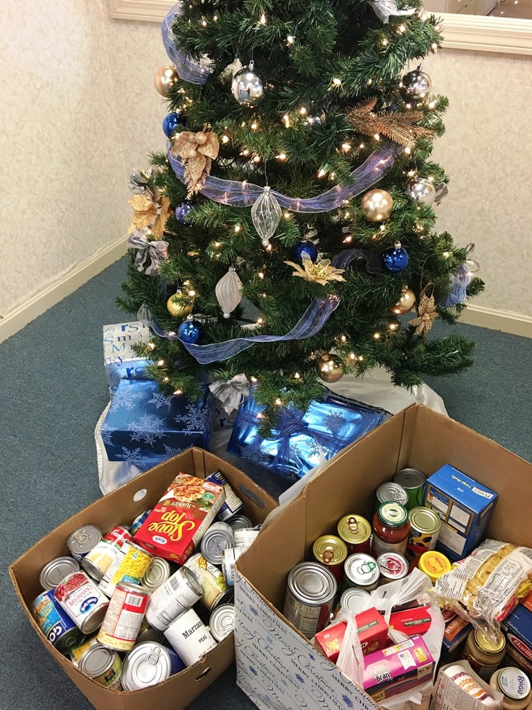 Boxes filled with canned goods next to a decorated Christmas tree.