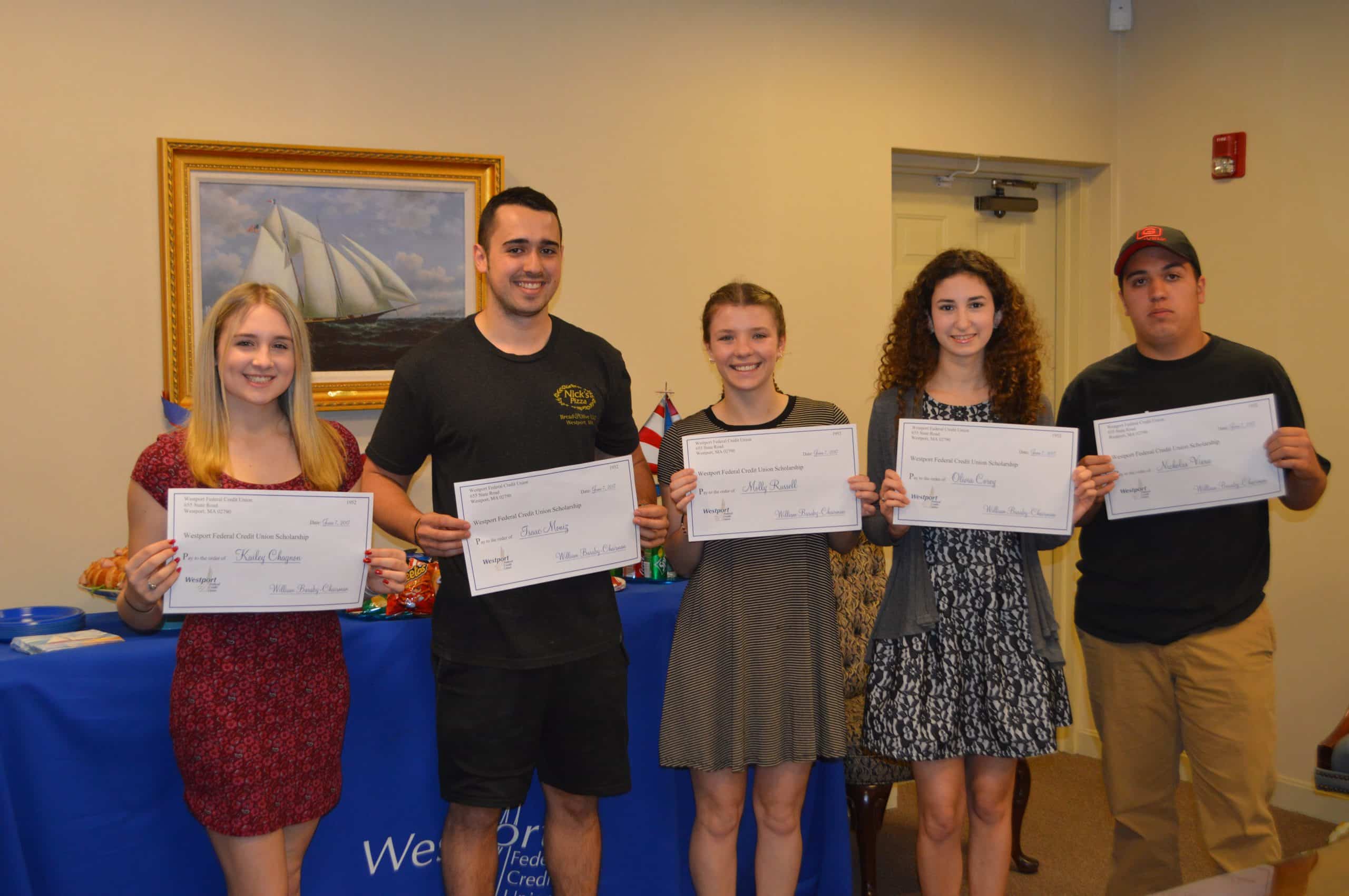 Five smiling young adults holding large scholarship checks at an awards event.