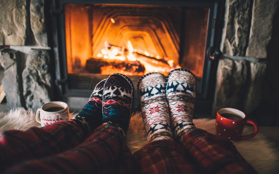 Two pairs of feet in patterned socks by a fireplace with hot drinks.